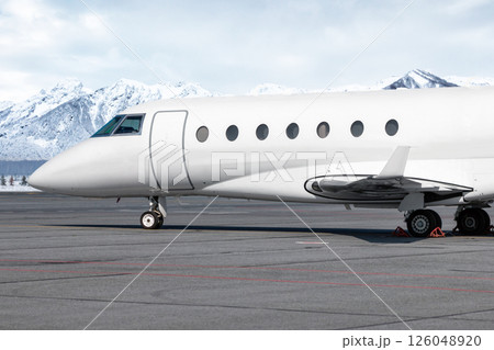 Close-up of the front of the luxury white corporate airplane at the winter airport on the background of high scenic snow capped mountains 126048920