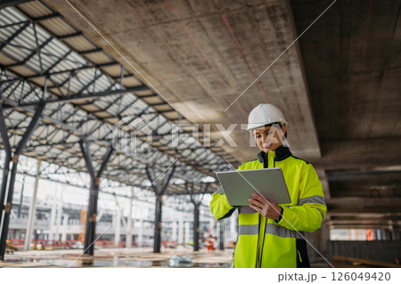 Female engineer checking building documentation on clipboard at construction site. 126049420