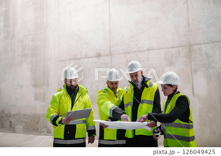 Team of engineers and construction workers reviewing blueprints, building site. Team of engineers and construction workers reviewing blueprints, building site. 126049425