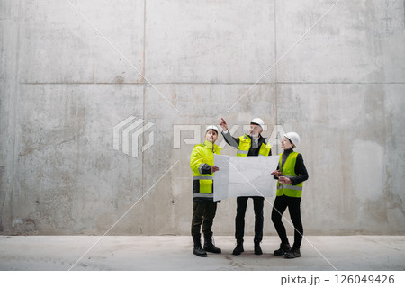Team of engineers and construction workers reviewing blueprints, building site. 126049426