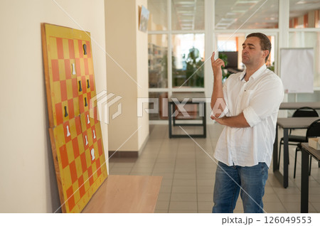 Caucasian man standing at wall mounted magnetic chessboard demonstration. Caucasian man standing at wall mounted magnetic chessboard demonstration. 126049553