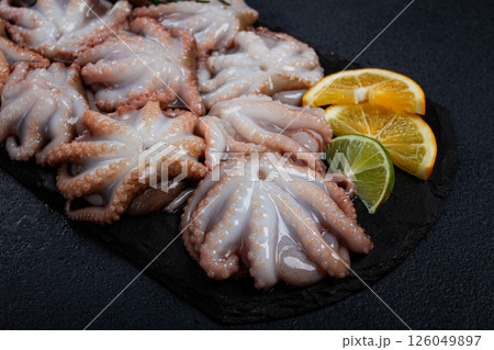 Fresh baby octopus, on black slate, with lemon and greenery, top view, no people, 126049897