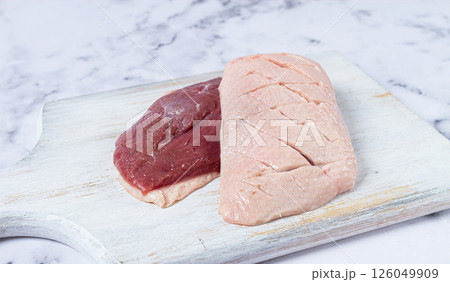 Fresh raw duck breasts, laid out on a wooden cutting board, on a white marble surface Fresh raw duck breasts, laid out on a wooden cutting board, on a white marble surface 126049909