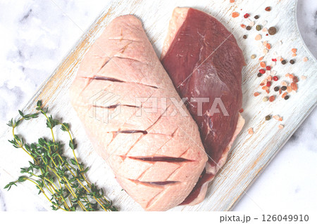Fresh raw duck breasts, spread on a wooden cutting board, with herbs and spices, on a white marble surface Fresh raw duck breasts, spread on a wooden cutting board, with herbs and spices, on a white marble surface 126049910