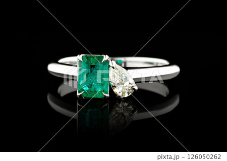 silver or gold ring with emerald stone and diamonds on black background 126050262