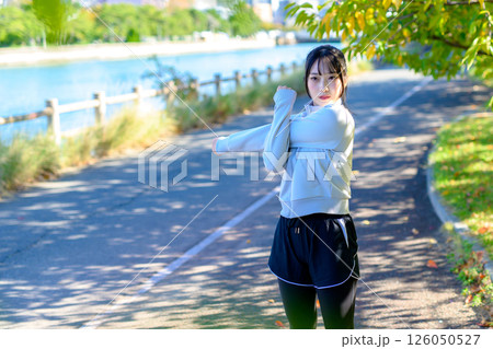 木漏れ日の道で肩や肩甲骨ストレッチをするかっこいい女性　準備運動　エクササイズ　トリミングアップ 126050527