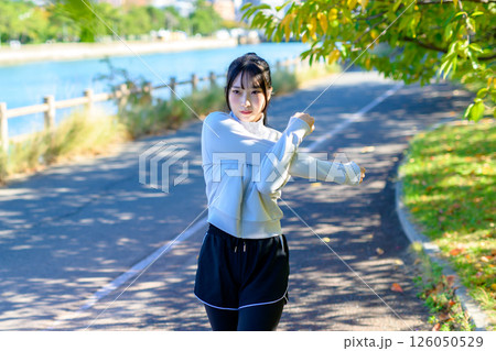 木漏れ日の道で肩や肩甲骨ストレッチをするかっこいい女性　準備運動　エクササイズ　トリミングアップ 126050529