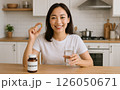 自宅のキッチンで水と一緒に栄養補助食品を摂取し、健康と日々のセルフケアを体現する笑顔の女性。 126050671