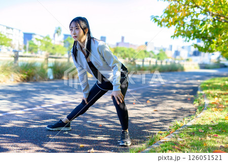 川沿いの歩道で脚のストレッチをするかっこいい女性　屈伸開脚　ダイエット　散歩　運動　 126051521