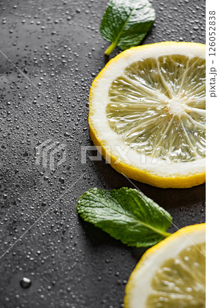 Fresh juicy lemon slices on a black background. Cocktail ingredient - mint leaves and lemon. Water drops on ripe lemon. Food background. Vertical photo. 126052838