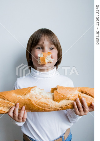Young caucasian child enjoying a french baguette with playful expression against a white background Young caucasian child enjoying a french baguette with playful expression against a white background 126053340