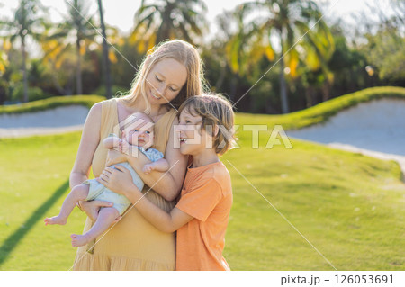 Mother, older son, and newborn baby on a meadow in the park. Family spending quality time together in nature. Parenthood, love, and family bond concept Mother, older son, and newborn baby on a meadow in the park. Family spending quality time together in nature. Parenthood, love, and family bond concept 126053691