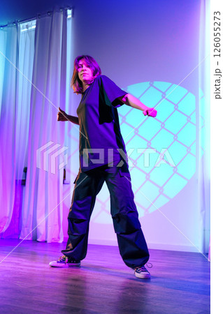 Dynamic dance performance by a female artist on stage during a colorful light show in an urban setting 126055273