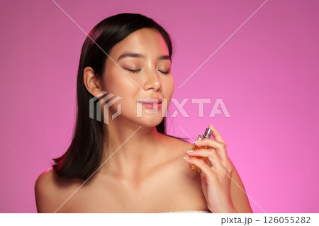 Woman applying fragrance in a beauty studio with pink lighting during a self-care routine 126055282