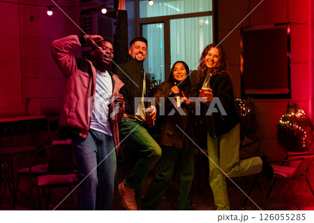 Group of friends celebrating joyfully at party with drinks in festive outdoor setting at night 126055285