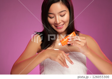 Woman applying skincare product on her hand against a purple backdrop during a beauty routine 126055300