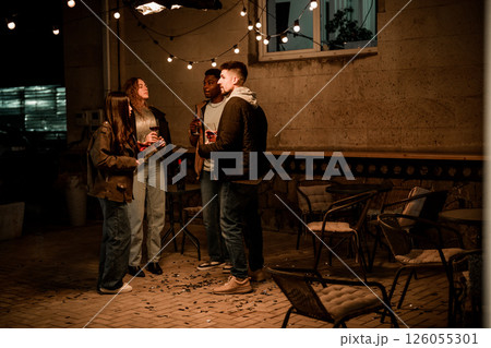 Friends enjoy an evening gathering outdoors under fairy lights in a lively atmosphere Friends enjoy an evening gathering outdoors under fairy lights in a lively atmosphere 126055301