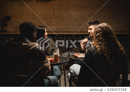 Friends enjoy a casual meal in a cozy setting at night in an urban area 126055388