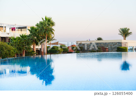 Stunning infinity pool reflecting palm trees at sunset by a luxury resort 126055400