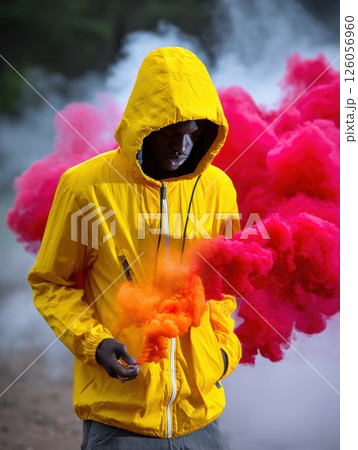 Model wearing yellow hooded jacket holding orange smoke bomb creating colorful smoke effect 126056960