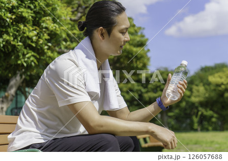 公園のベンチに座って水分補給をする若い男性 126057688