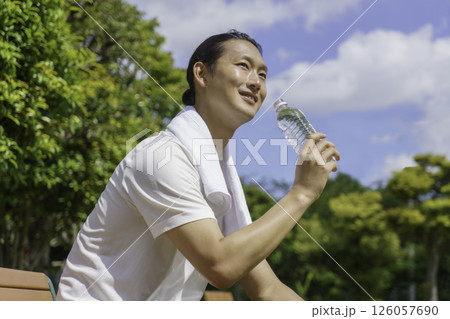公園のベンチに座って水分補給をする若い男性 126057690