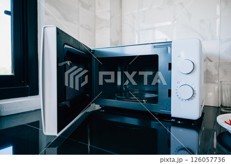 An open microwave oven door on a sleek kitchen tabletop presenting modern technology and design in household appliances. Perfect for showcasing contemporary kitchen equipment. An open microwave oven door on a sleek kitchen tabletop presenting modern technology and design in household appliances. Perfect for showcasing contemporary kitchen equipment. 126057736