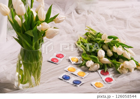 Colorful condoms lying on a background of white tulips 126058544