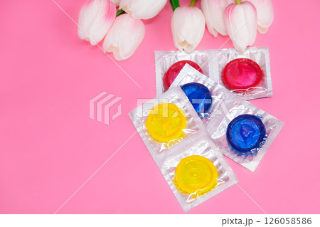 Colorful condoms lying on pink background with tulips, space for text 126058586