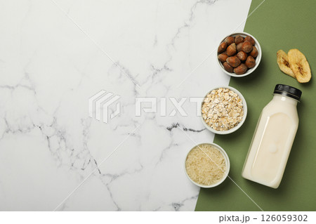 Bottle of alternative milk and herbal ingredients on white and green background, space for text 126059302