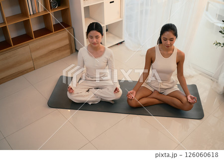 Calm and focused mother and daughter practicing yoga together in a peaceful indoor Calm and focused mother and daughter practicing yoga together in a peaceful indoor 126060618