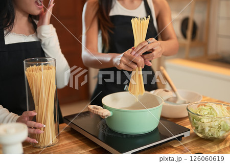 Mother breaking dry spaghetti over a pot while her teenage daughter reacts with surprise Mother breaking dry spaghetti over a pot while her teenage daughter reacts with surprise 126060619