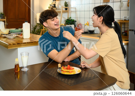 Loving young couple feeding each other pancakes while enjoying breakfast in a kitchen Loving young couple feeding each other pancakes while enjoying breakfast in a kitchen 126060644