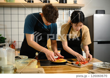 Man and woman decorating pancakes with fruit toppings in a kitchen 126060670
