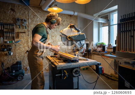 Skilled carpenter use miter saw, measure and trim wood beams in workshop. Handyman precision cut Skilled carpenter use miter saw, measure and trim wood beams in workshop. Handyman precision cut 126060693