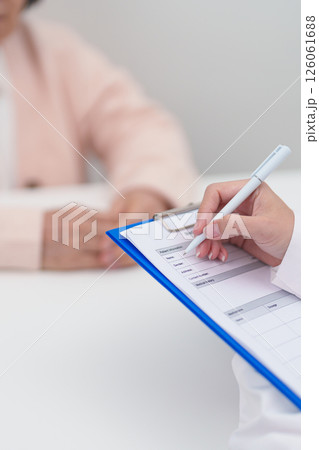 senior woman consulting with doctor in hospital. Elderly patient talking and sharing disease. Doctor listens, asking question and taking note. medical consultation and geriatric Healthcare concept 126061688
