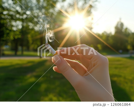 Woman holding a lit cigarette at sunset in a park, addiction and bad habits 126061864