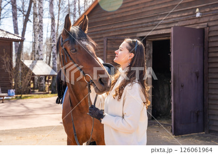 Young woman standing beside a horse at a stable. Concept of emotional connection between humans and animals. 126061964
