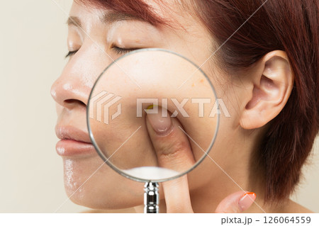女性の頬をルーペで拡大している。 126064559
