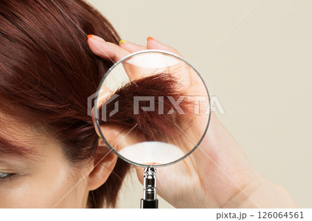 女性の髪の毛先をルーペで拡大している。 126064561