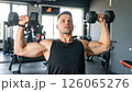 Athletic man performing shoulder press with dumbbells in modern gym, showcasing strength and focus 126065276