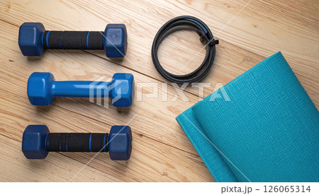 Blue dumbbells, resistance band, and yoga mat on wooden floor for shoulder press workout 126065314