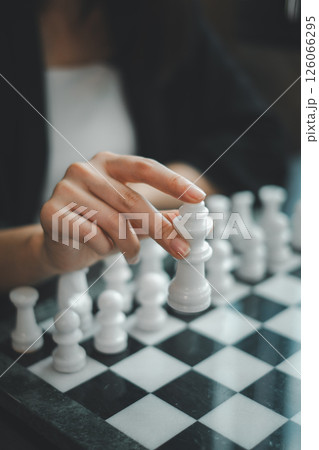 A focused hand moves a chess piece on a classic black and white chessboard, capturing the essence of strategic gameplay. 126066295