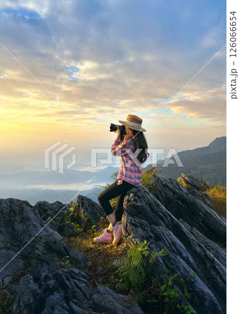 Traveller sitting on the rock and holding camera take photo at Doi pha mon mountains in Chiang rai, Thailand. 126066654