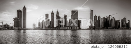 Monochrome city skyline with tall skyscrapers reflecting on calm water under a cloudy sky, Dubai Marina bay UAE Monochrome city skyline with tall skyscrapers reflecting on calm water under a cloudy sky, Dubai Marina bay UAE 126066812