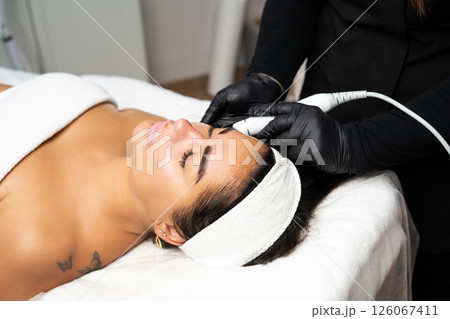 Close-up portrait of a beautiful woman with closed eyes and apparatus for skin rejuvenation. Beauty salon procedures. RF lifting. Microcurrents. Close-up portrait of a beautiful woman with closed eyes and apparatus for skin rejuvenation. Beauty salon procedures. RF lifting. Microcurrents. 126067411