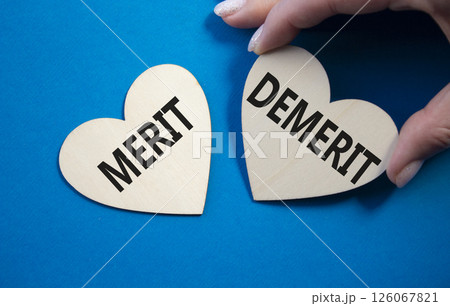 Merit or Demerit symbol. Concept word Merit or Demerit on wooden hearts. Businessman hand. Beautiful blue background. Business and Merit or Demerit concept. Copy space 126067821
