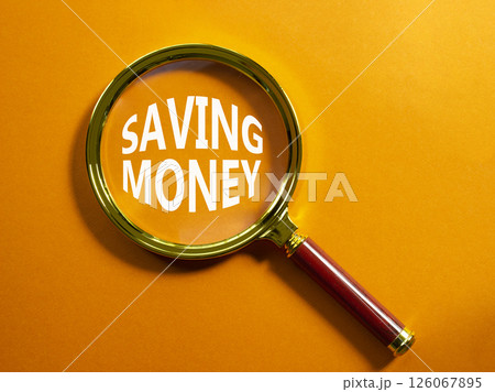 Saving Money symbol. Concept words Saving Money on magnifying glass. Beautiful orange background. Business and Saving Money concept. Copy space. Saving Money symbol. Concept words Saving Money on magnifying glass. Beautiful orange background. Business and Saving Money concept. Copy space. 126067895
