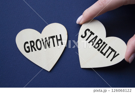 Growth and Stability symbol. Concept word Growth and Stability on wooden hearts. Businessman hand. Beautiful deep blue background. Business and Growth and Stability concept. Copy space 126068122