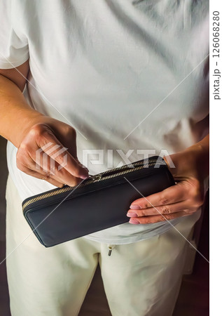 Female figure is holding a black wallet and preparing to open it in a cozy indoor space. High quality photo Female figure is holding a black wallet and preparing to open it in a cozy indoor space. High quality photo 126068280